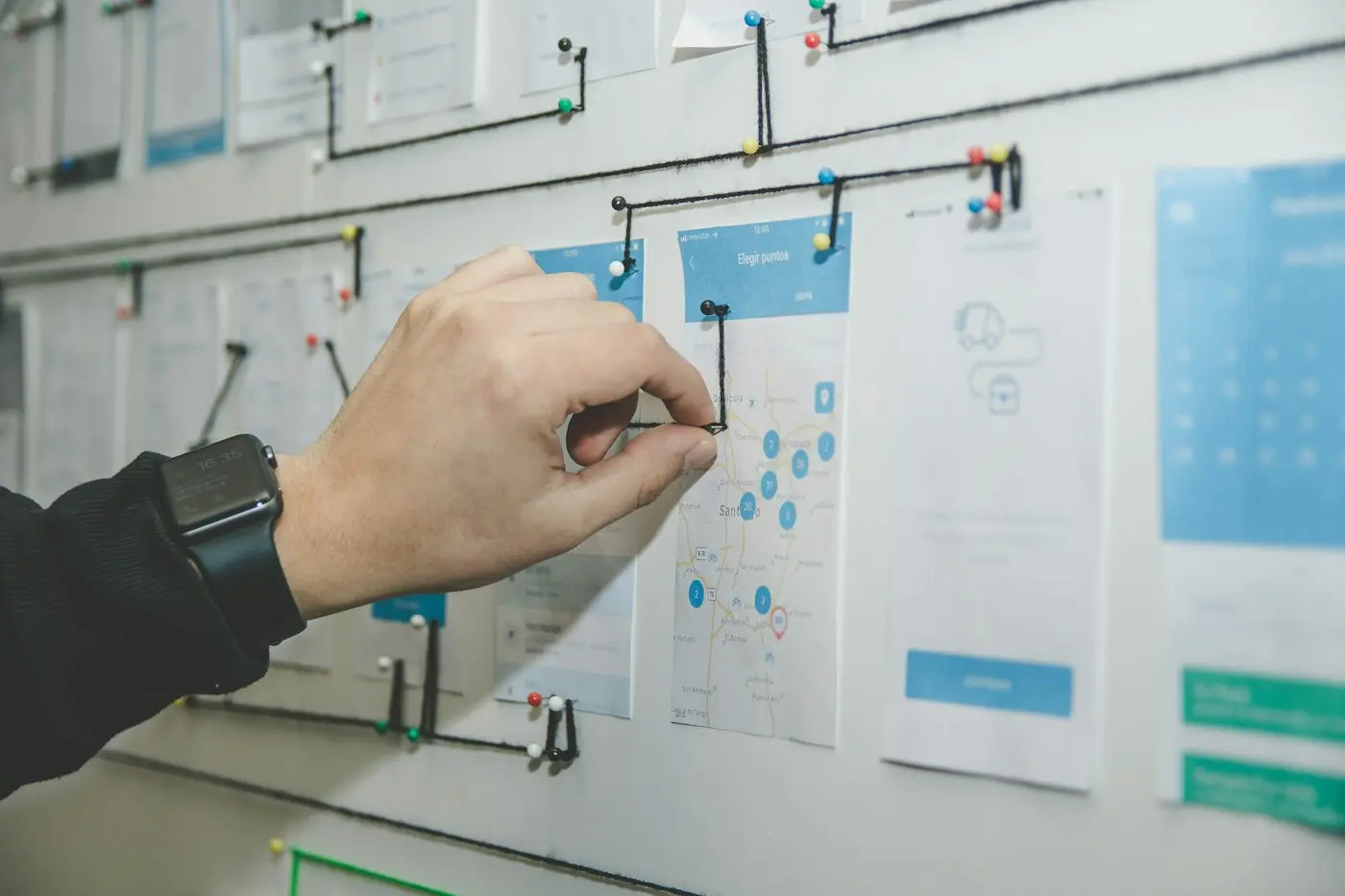 A hand placing a wireframe on a wall of interface sketches.